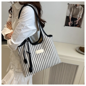 Detail of a large black and white striped canvas tote bag with leather straps on a model