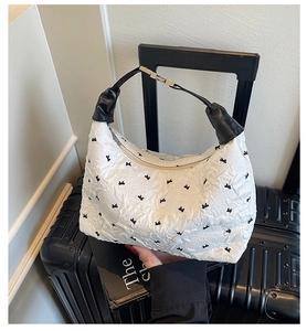 Close-up of white textured shoulder bag with black bow print and leather handle details