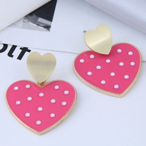 Détail de boucles d'oreilles cœur dorées avec émail rose et motifs à pois blancs