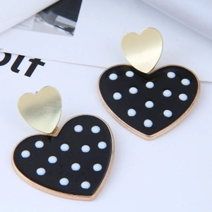 Détail de boucles d'oreilles cœur en émail noir avec des motifs à pois blancs