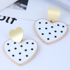 Détail de boucles d'oreilles cœur en or avec émail blanc et pois noirs pour femme