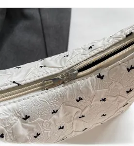 Detail of silver metal zipper on white pleated bag with black bow print and texture
