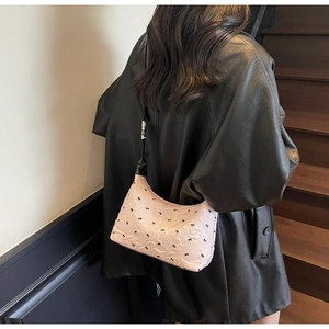 Close-up of pink shoulder bag featuring black bow patterns and slim strap detail