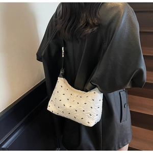 Chic white crescent shoulder bag with black bow embroidery worn by a model in black leather jacket