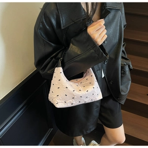 Detail of light pink shoulder bag featuring black bow embroidery and textured fabric