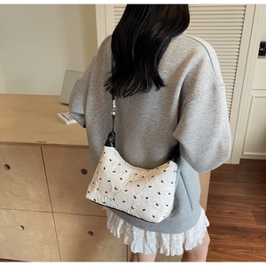 Detail of white quilted handbag with floral embroidery and black shoulder strap