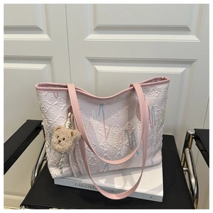 Detail of pink and white tote bag with embossed texture and a cute plush bear charm