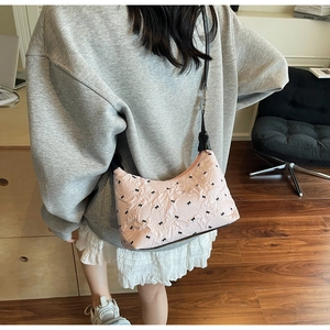 Pink quilted shoulder bag with black bow print worn by a model in a natural setting