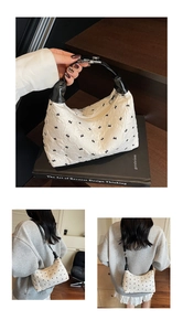 Detail of white pleated handbag featuring delicate black bow embroidery and leather strap