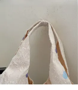 Détail du sac cabas en toile blanche avec broderies florales et texture à franges