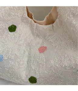 Détail d'un sac cabas beige capitonné avec broderies florales colorées et tissu en peluche doux