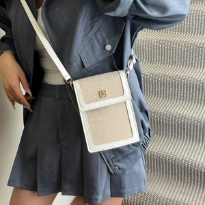 Minimalist beige canvas bucket bag with floral metal clasp worn with a grey outfit
