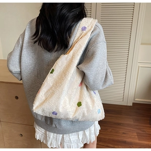 Detail of cream tote bag with colorful embroidery and textured fabric on shoulder