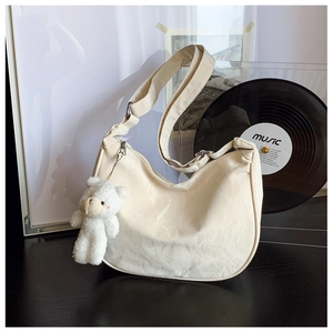 Detail of cream croissant bag with pleated texture and a cute white plush bear charm