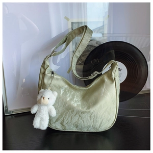 Close-up of light green pleated hobo bag with a plush bear charm and adjustable strap