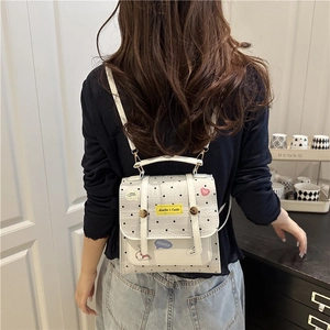 White mini backpack with black polka dots and cartoon patches worn by a model