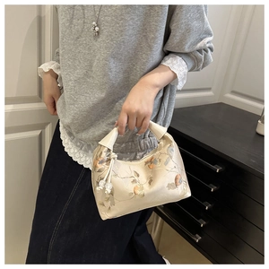 Detailed close-up of bird and flower embroidery on a beige canvas shoulder bag