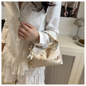 Detail of floral embroidery and unique knotted handle on a cream canvas shoulder bag