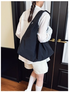 Detailed back view of a large black nylon tote bag worn by a model in a minimalist setting