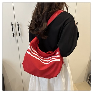 Détail du sac bandoulière en toile rouge avec trois rayures blanches et sangle noire