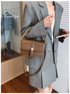Détail d'un sac bandoulière en cuir marron avec cadenas doré et chaîne sur un blazer gris
