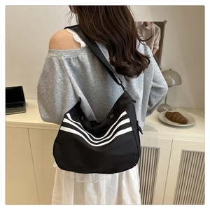 Détail d'un grand sac bandoulière avec trois bandes blanches sur tissu noir