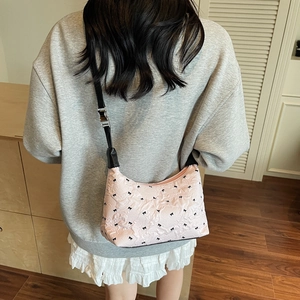 Pink hobo shoulder bag with black bow embroidery and adjustable strap on a model
