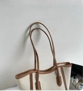 Detail of a minimalist cream tote bag featuring brown leather straps on a modern desk setup