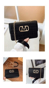 Detalle de bolso bandolera negro con diseño de cocodrilo, hebilla M dorada y correa de cadena