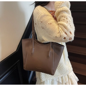 Detail view of dark brown tote bag on model showing fine leather texture and golden text