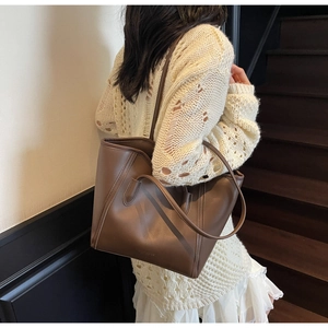 Detail of dark brown leather tote bag with vertical stitching on model in knit sweater