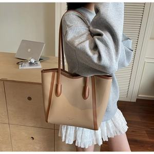 Detail of khaki leather tote bag with brown trim and shoulder straps in a home setting