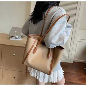 Close-up of beige leather tote bag with brown trim and shoulder strap on model