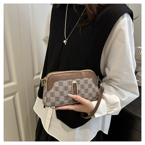 Detail of grey jacquard crossbody bag with brown leather trim and metal clasp on model