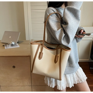 Detail of elegant cream tote bag with brown trim carried by a model in office setting
