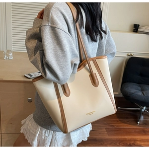 Detail of a minimalist beige leather tote bag with brown trim and shoulder strap