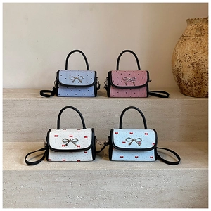 Mini pleated crossbody bags with bow hardware on light stone display stand