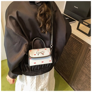 Detail of white mini crossbody bag with red bow prints and silver metallic buckle