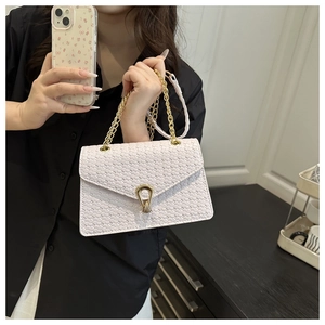 Détail du sac enveloppe tressé avec fermoir doré et bandoulière en chaîne