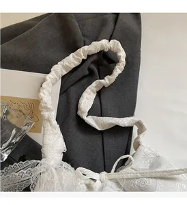 Detail of white lace tote bag with floral embroidery and ruched strap on a grey blazer