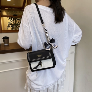 Sac bandoulière carré noir et blanc chic avec foulard en soie et pompon sur un mannequin