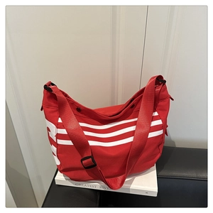 Détail du sac bandoulière en toile rouge avec trois bandes blanches et sangle réglable