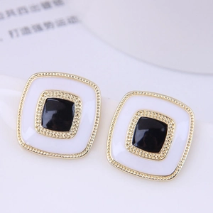 Macro detail of geometric square earrings with black and white enamel in gold finish