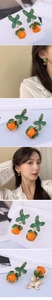 Detailed view of persimmon pendant earrings with green enamel leaves and orange glass beads