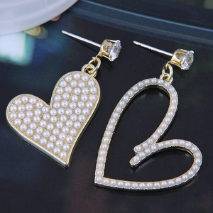 Detail of asymmetric heart earrings with pearls and zircon on a dark background