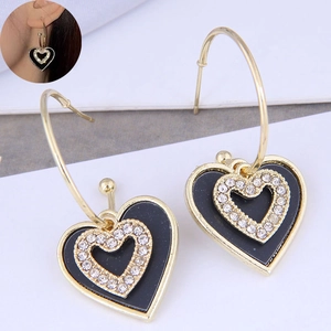 Detail of heart-shaped gold earrings with black enamel and sparkling rhinestones