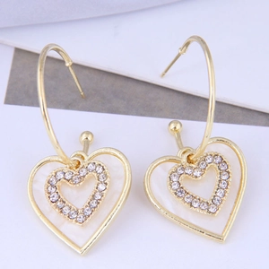 Macro detail of gold heart drop earrings with white shell inlay and sparkling crystals