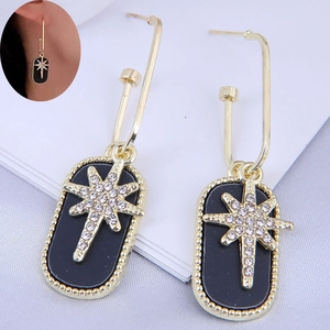 Detail of drop earrings with black oval pendant and sparkling gold starburst