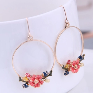 Detail of gold floral hoop earrings with pink enamel flowers on a white ceramic cup