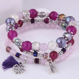 Detail of triple-layer beaded bracelet with purple tassels, clover charm, and Love pendant